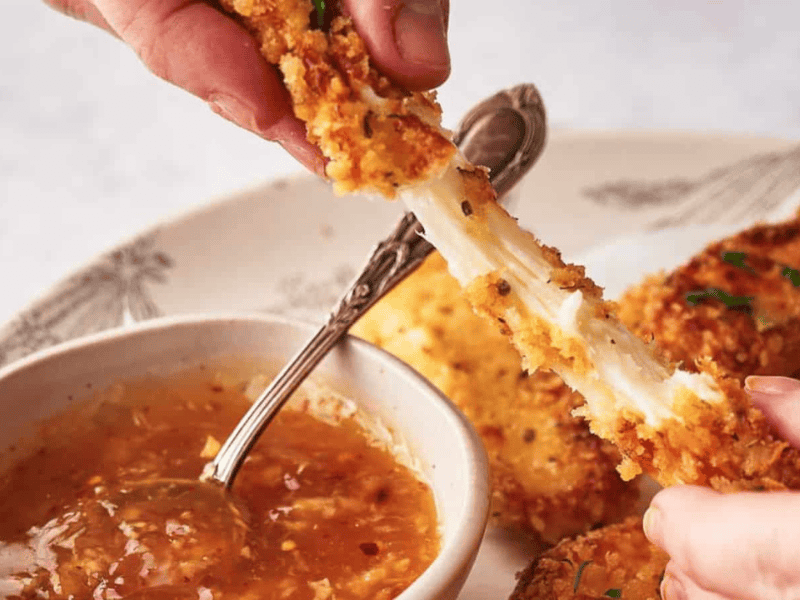 Someone pulling a mozzarella stick apart and showing the stretchy cheese.