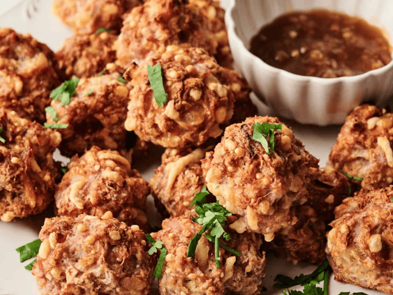 Plate of crispy fried dumplings with chopped herbs, served with a bowl of brown dipping sauce.