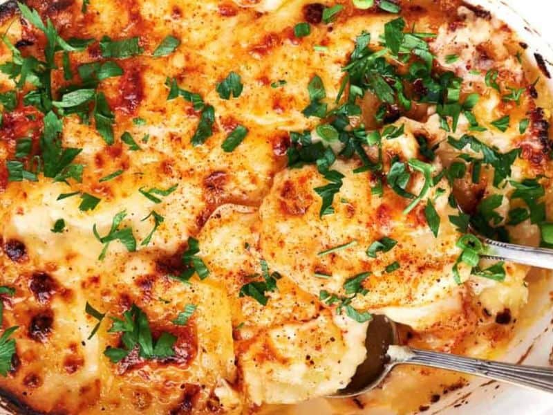 Cheesy potato casserole in a white dish with a fork.