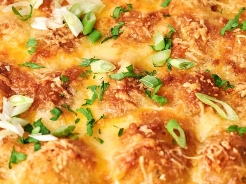 Close-up of a tater tot breakfast casserole topped with melted cheese, sliced green onions, and chopped herbs.