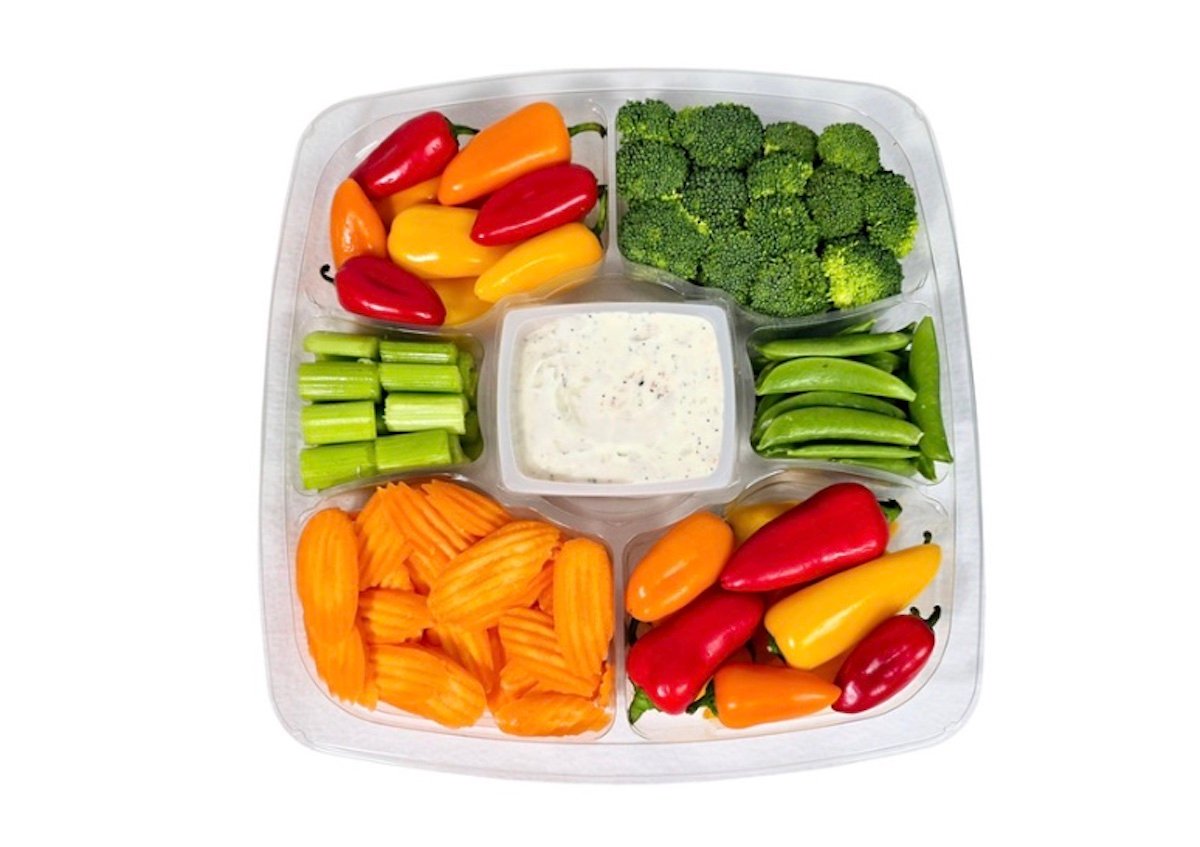 A vegetable tray with sections of baby bell peppers, broccoli florets, celery sticks, snap peas, crinkle-cut carrot slices, and a central container of ranch dip.
