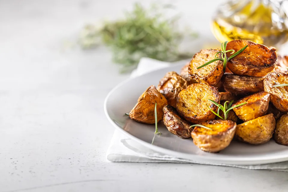 Golden baked potatoes on a white plate with rosemary