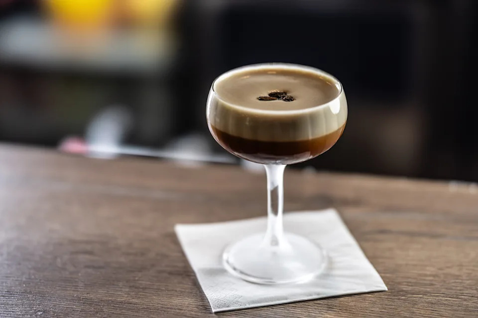 Cocktail glass with a layered espresso martini on a napkin, featuring a garnish of three coffee beans on top