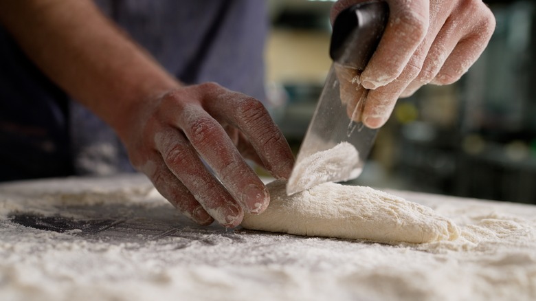 Hands dividing dough with bench scraper