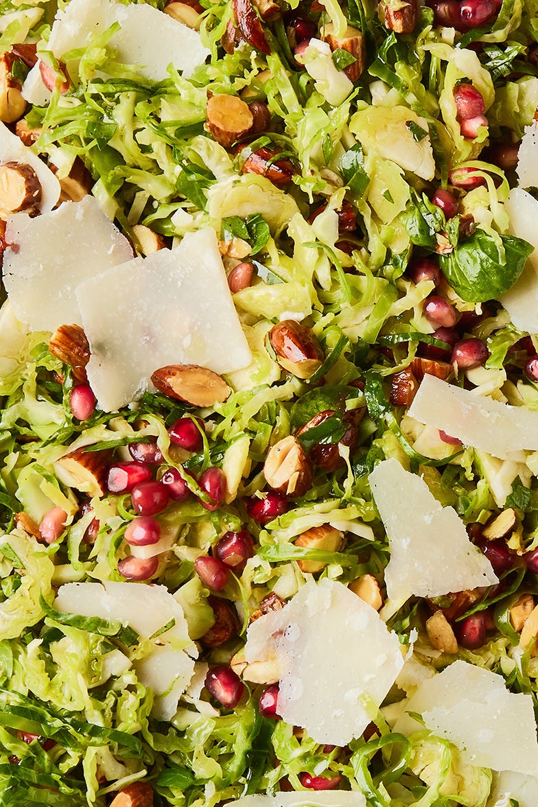 shaved brussels sprouts with pomegranates, shaved parmesan, and chopped toasted almonds in a white bowl
