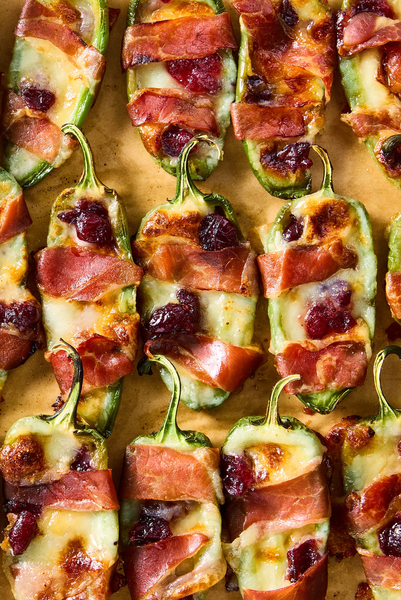 jalapeños stuffed with brie and wrapped with bacon, topped with cranberry sauce on a sheet tray