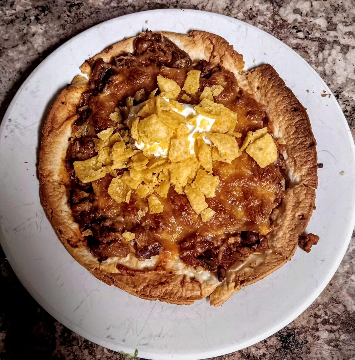 Homemade chili pizza with Mexican cheese blend, sour cream and crushed corn chips.