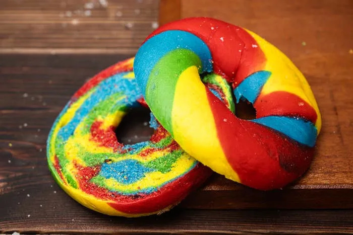 Two vibrant bagels with a swirl of rainbow colors displayed on a wooden surface