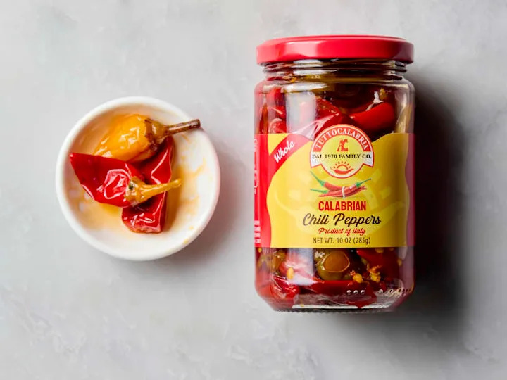 overhead shot of a small white bowl with three calabrian chilis, and the jar to the right of it.
