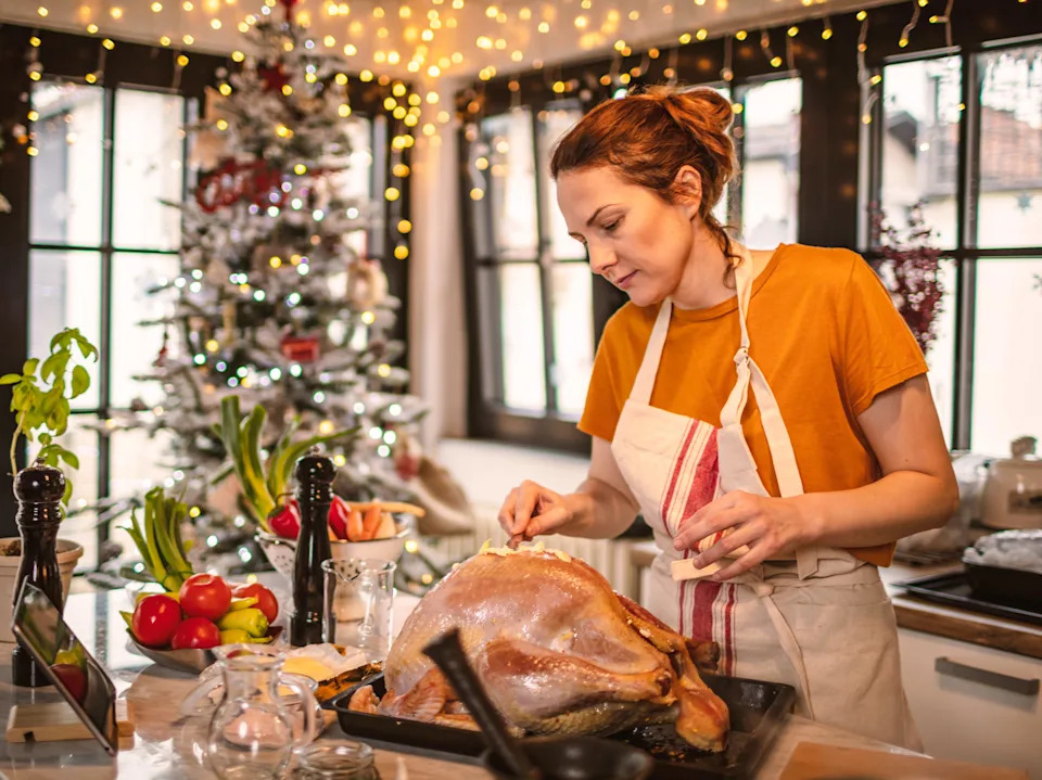 Young woman preparing stuffed turkey with vegetables and other ingredients for holidays