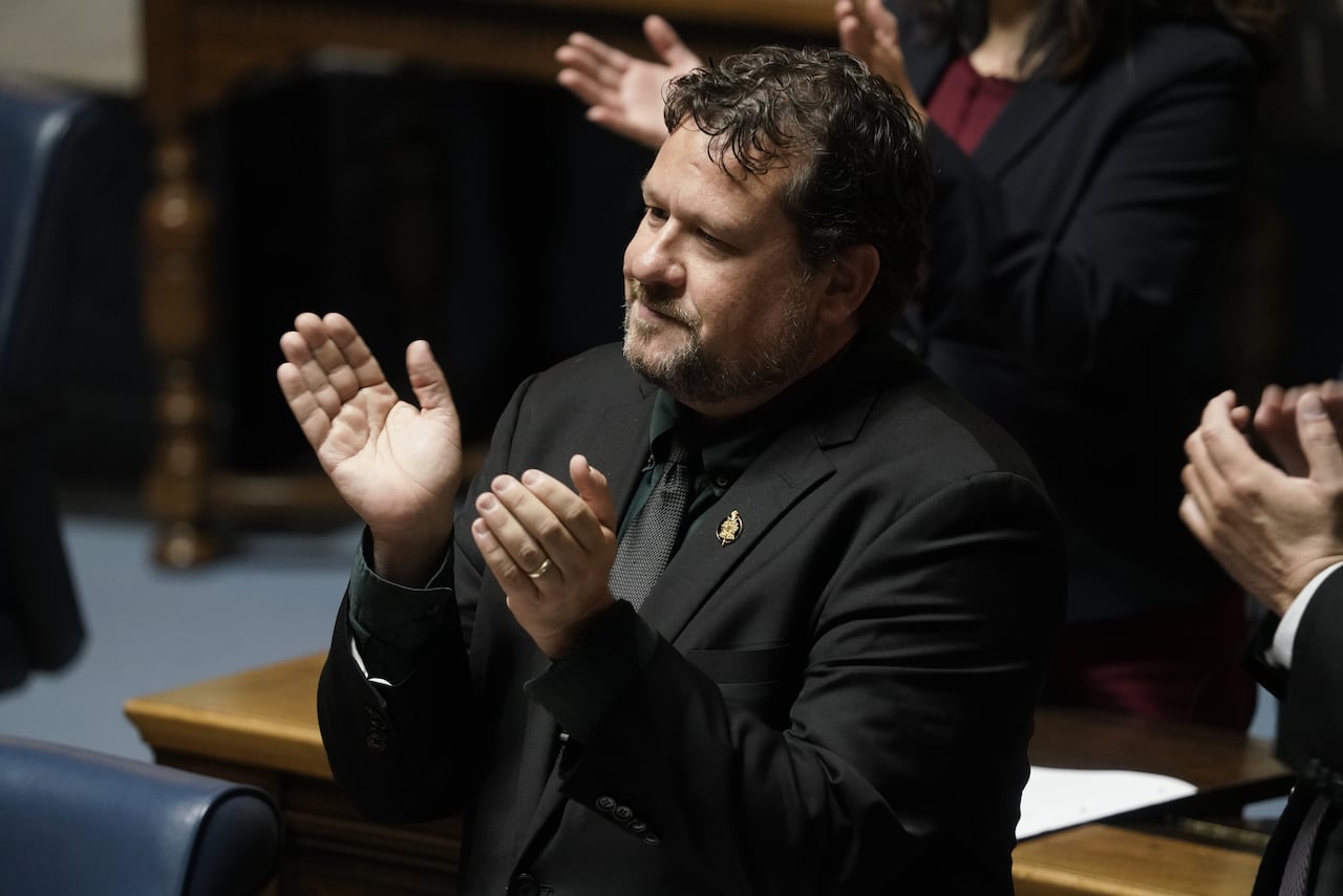 A man in a black suit claps.