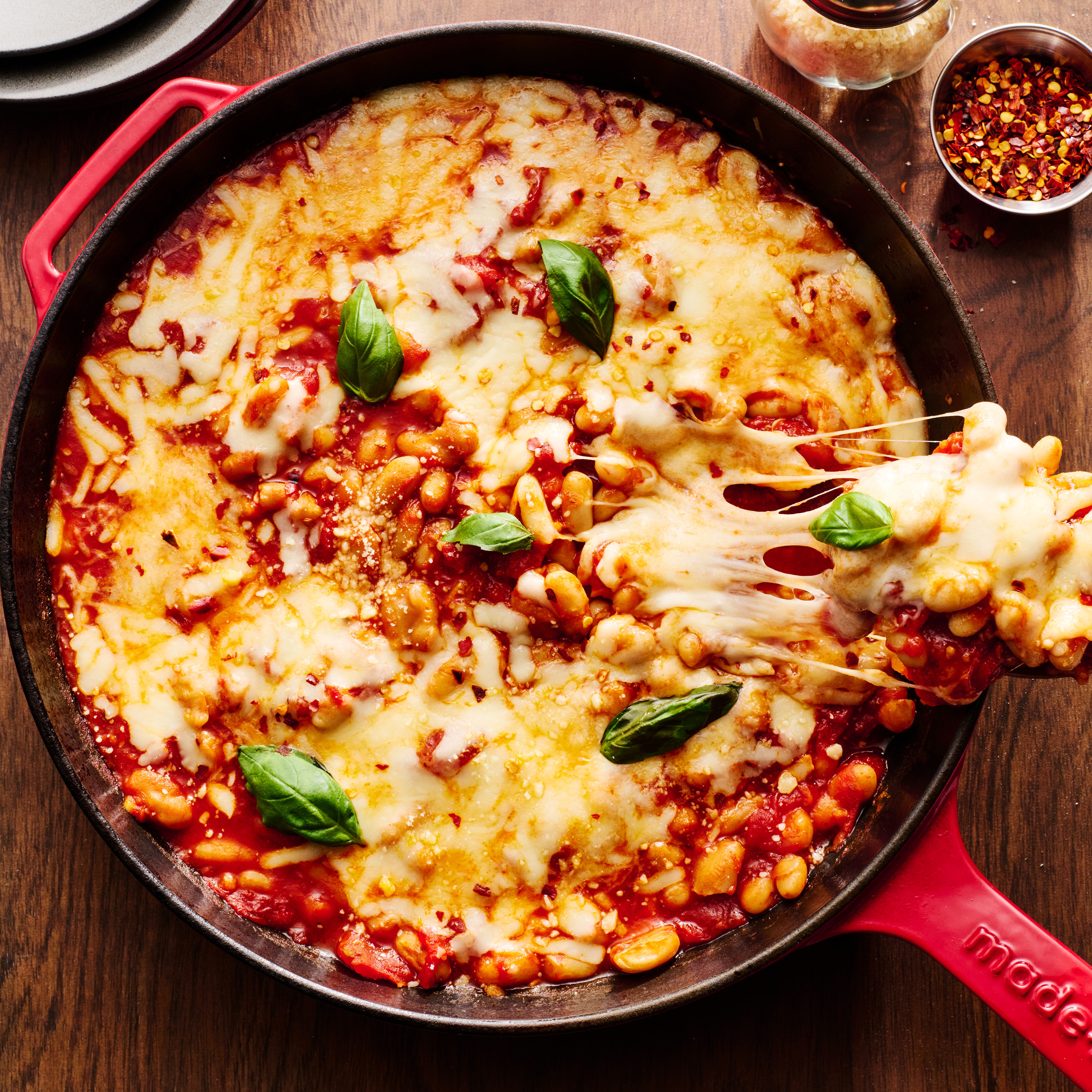pizza beans skillet topped with mozzarella and parmesan and basil with a scoop lifting out