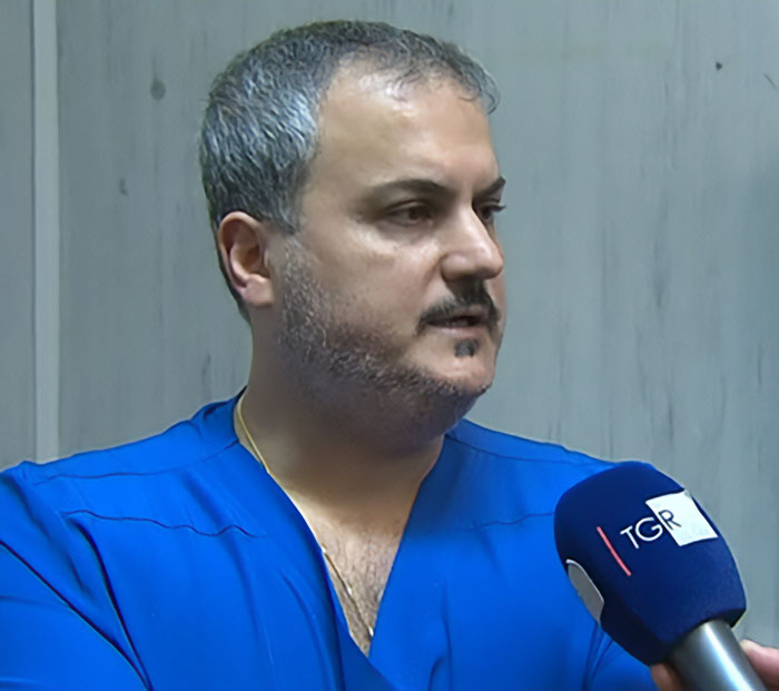 Doctor in blue scrubs interviewed by TGR microphone discussing town alert after fatal Christmas dinner incident in Italy.