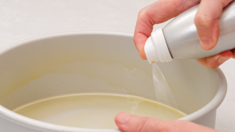 person spraying oil on pan