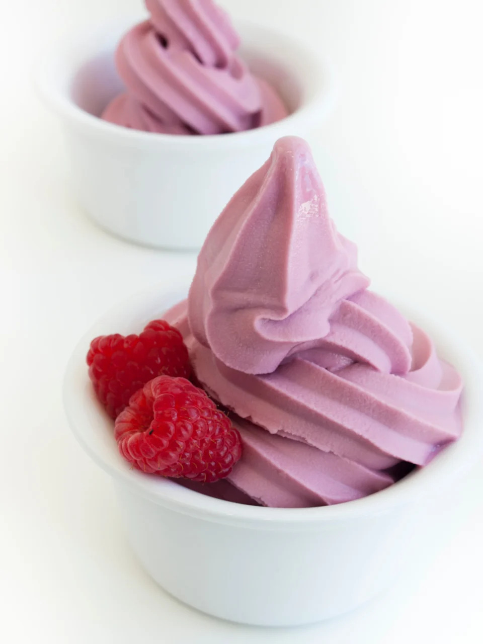 Two cups of swirled frozen yogurt topped with fresh raspberries in small white bowls
