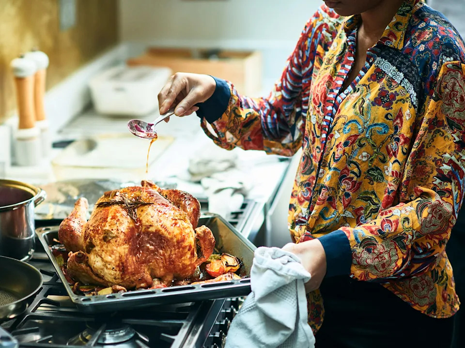 Woman holding spoon and pouring oil over roast chicken, cooking Christmas meal, family roast dinner, special occasion, home cooked food
