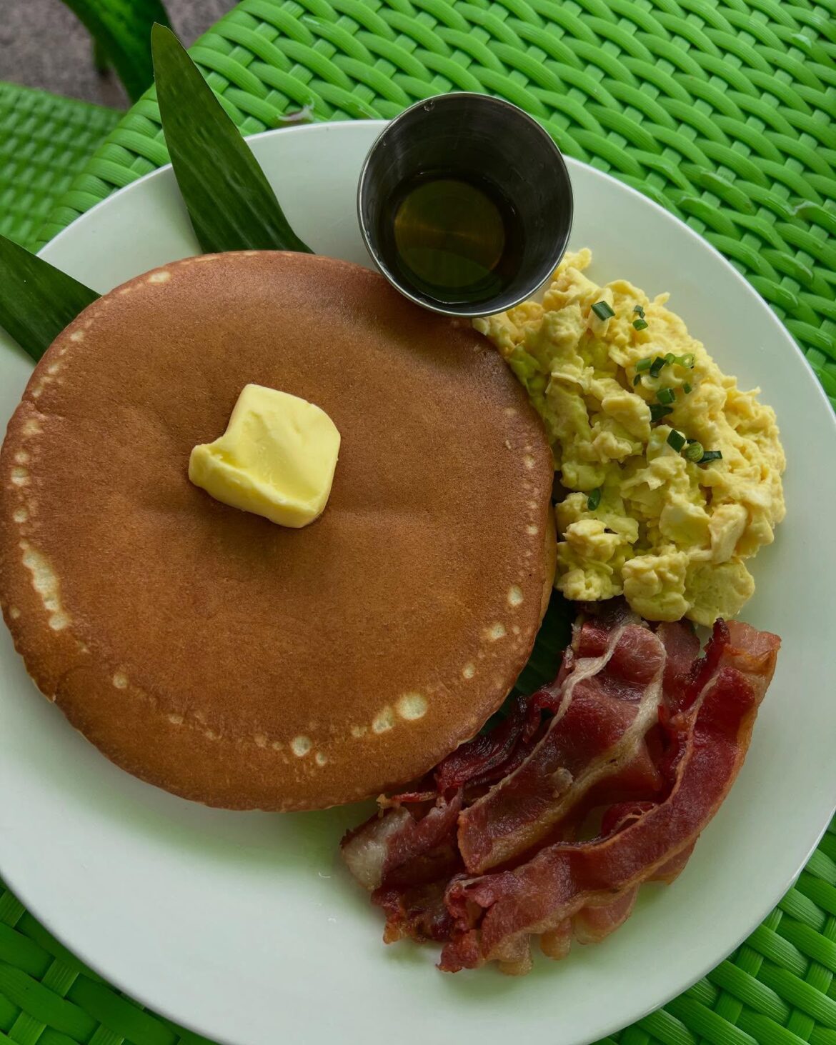 Fluffy buttermilk pancakes with butter and syrup, soft scrambled eggs with chives, and crispy bacon