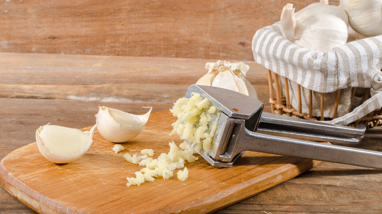 Garlic press and garlic on wooden board