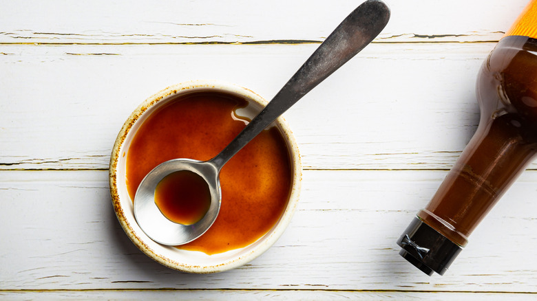 A top-down view of a small bowl with Worcestershire sauce in it with the bottle nearby.