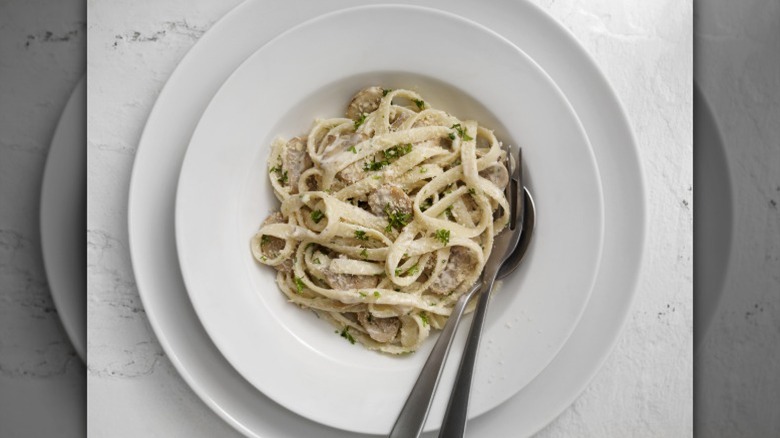 Alfredo pasta with mushroom served on a white plate with utensils on the side.