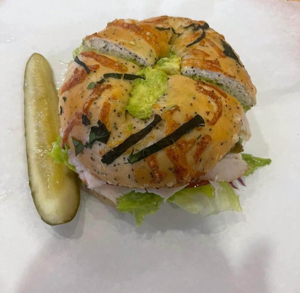 turkey sandwich on a bagel with a pickle on the side