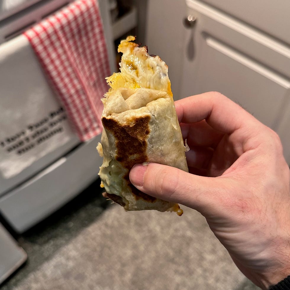 taco bell cheesy pulled burrito hand holding a rolled food item in a kitchen setting