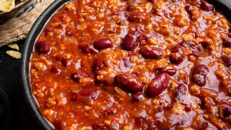 A close-up to a black bowl of chili con carne with beans in it.