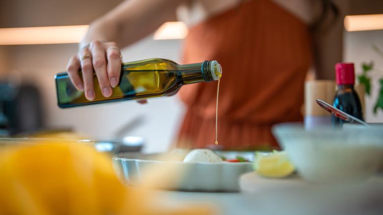 Woman pouring olive oil from bottle onto cheese on a plate