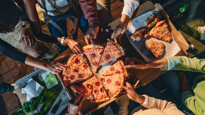 Friends sharing a pepperoni pizza that's been cut into slices in the box