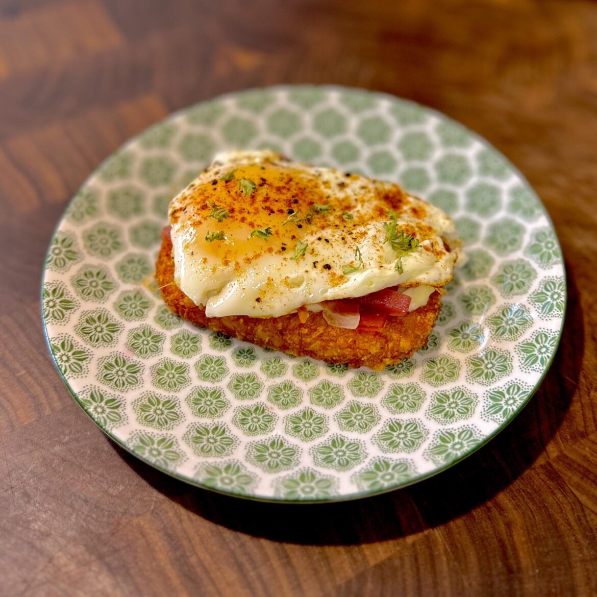 Open-faced hash brown slider with requeijão cremoso, Serrano ham, pickled red onions, fried egg, parsley, and paprika.