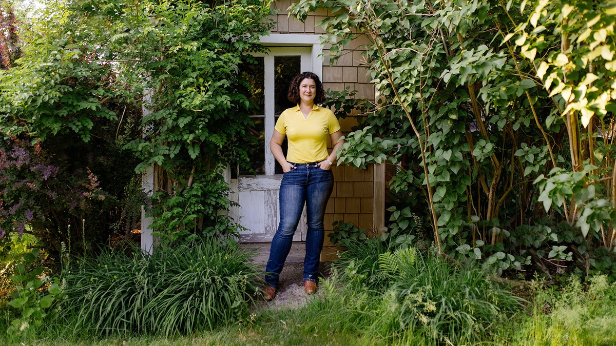 Nova Cadamatre stands in a yellow shirt and blue jeans in front of a home.