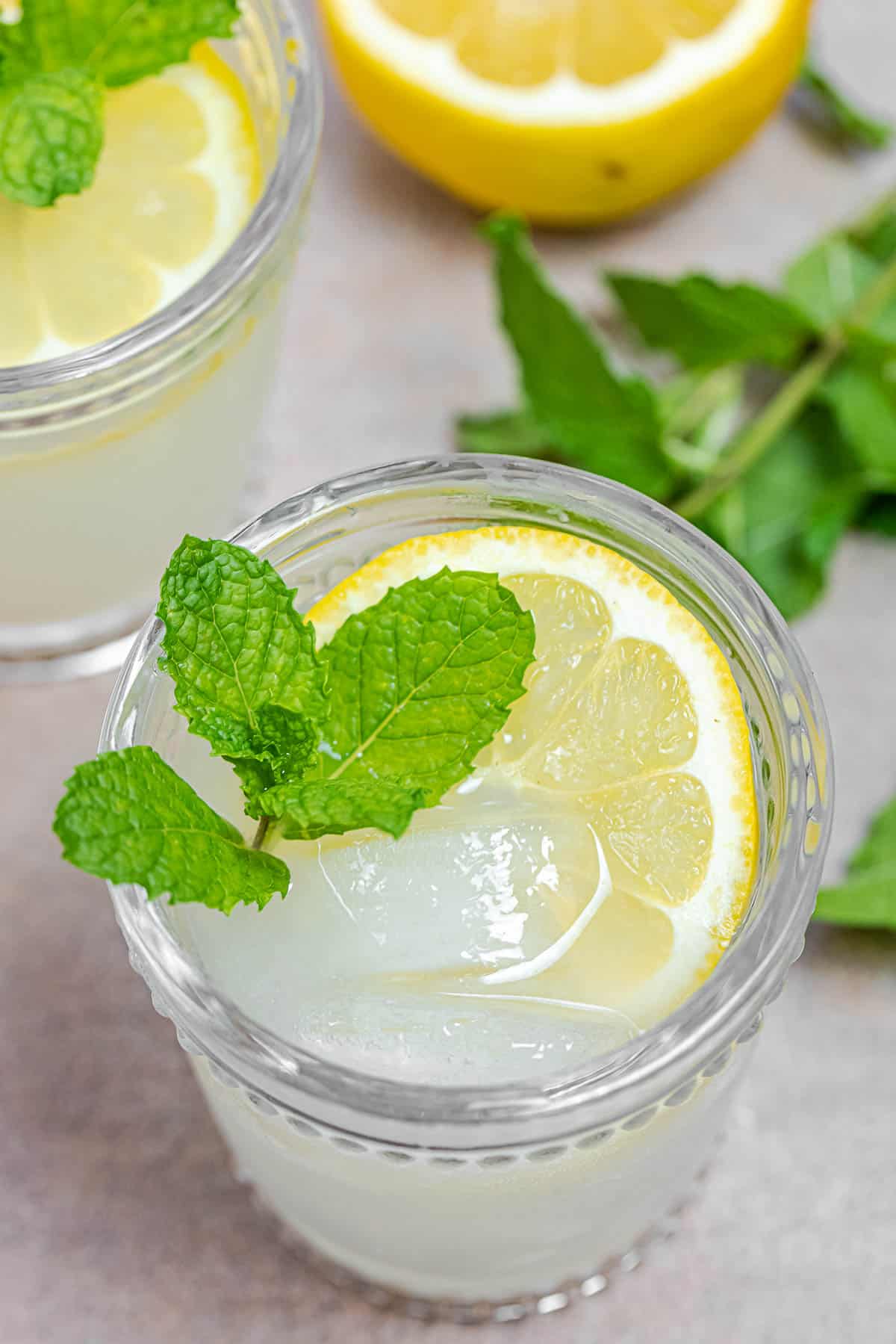 ouzo cocktail in a glass with fresh lemon, ice, and mint leaves. More lemon and mint in the background.