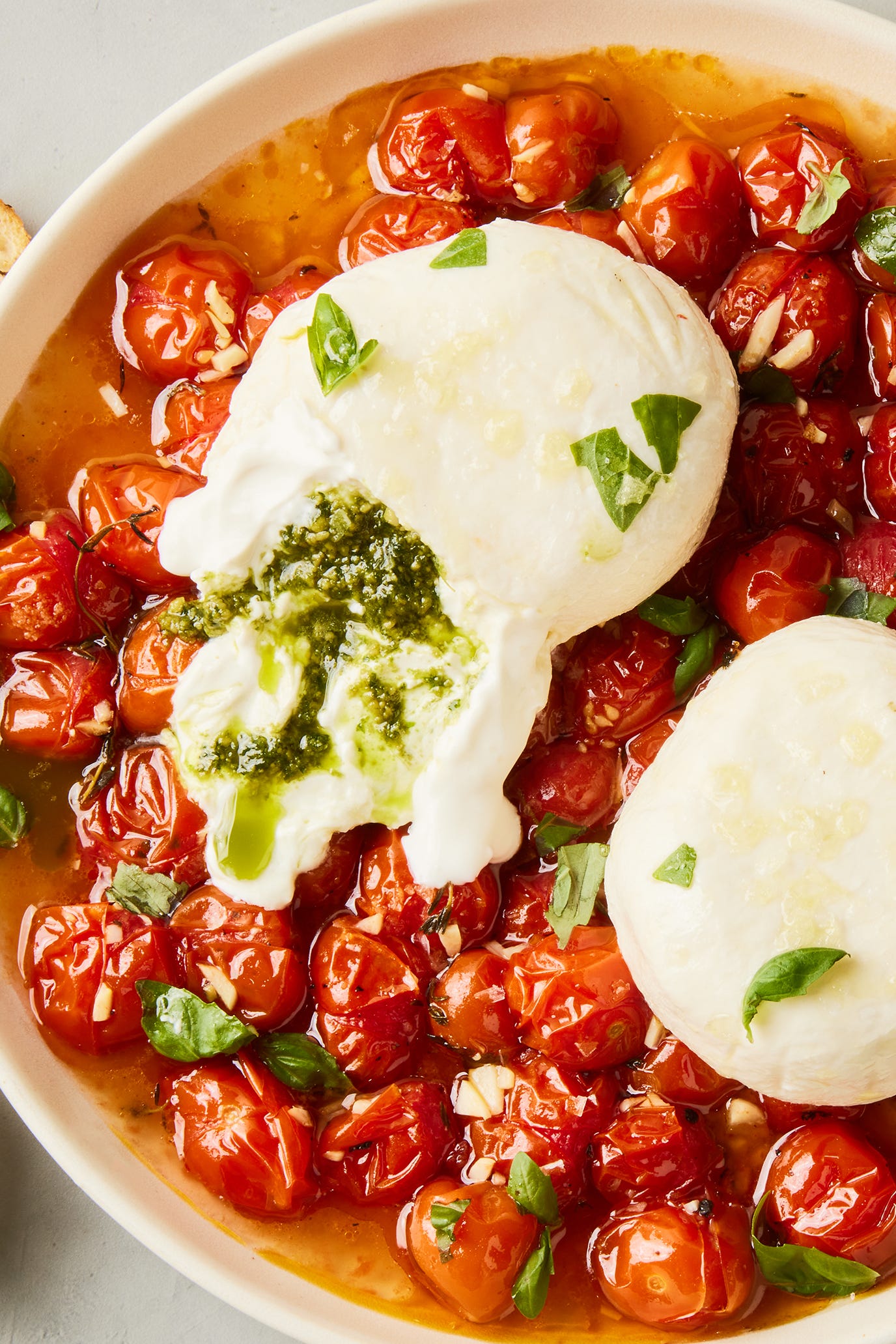 pesto stuffed burrata on top of burst cherry tomatoes with basil