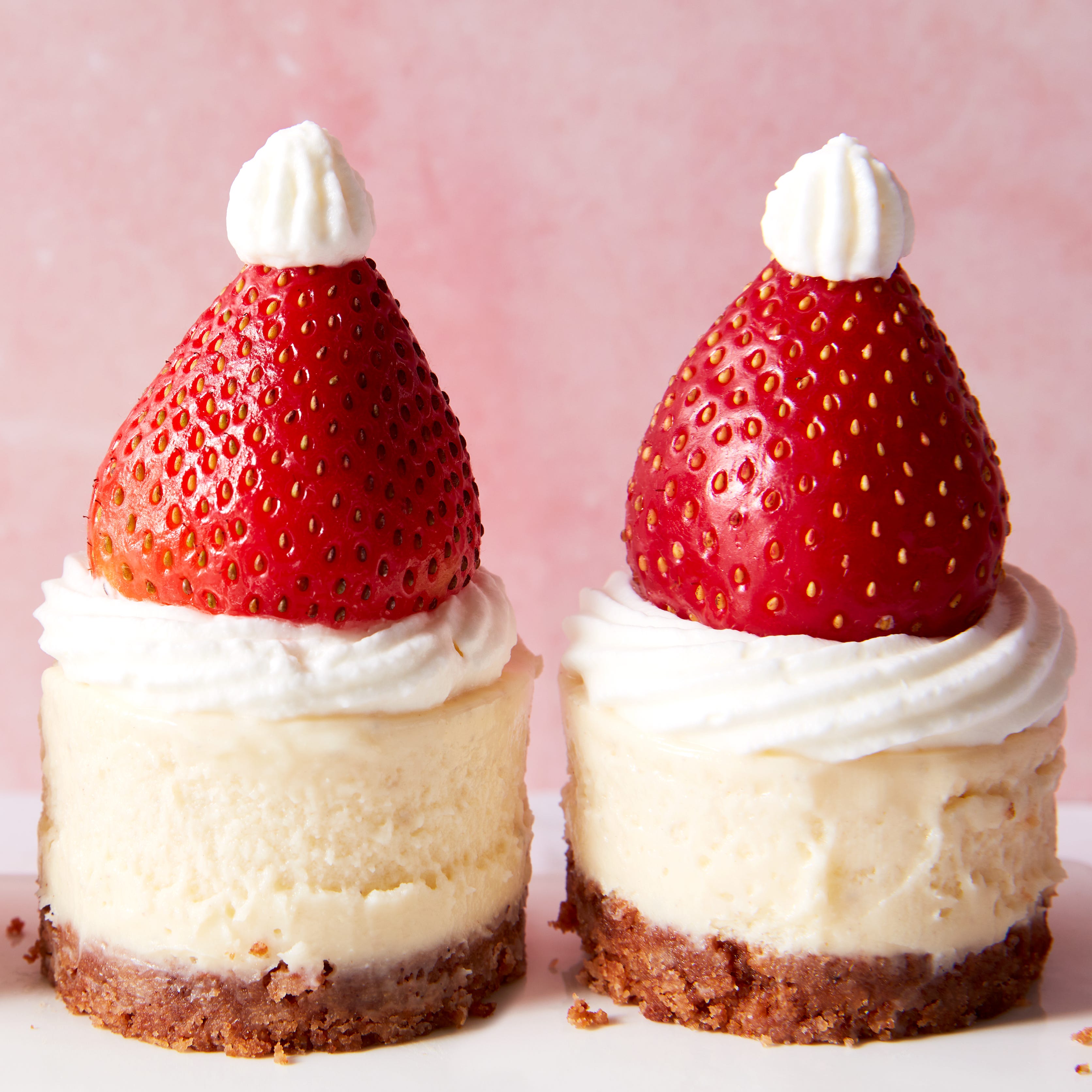 mini cheesecake bites topped with strawberries and whipped cream to look like a santa hat