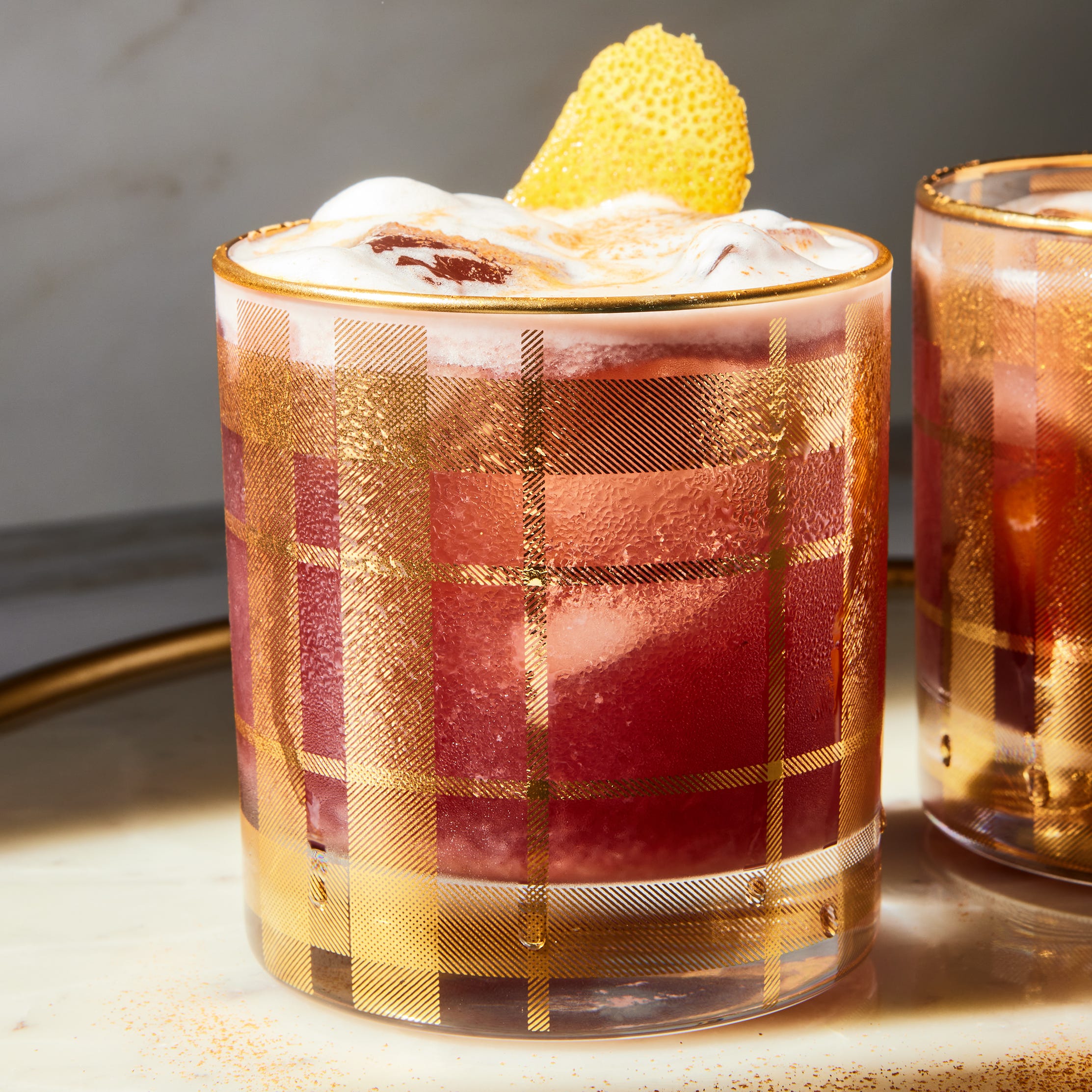 a red tinted sour garnished with an orange twist