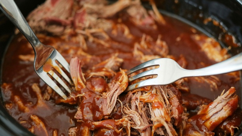 Using two forks to toss pulled pork in barbecue sauce