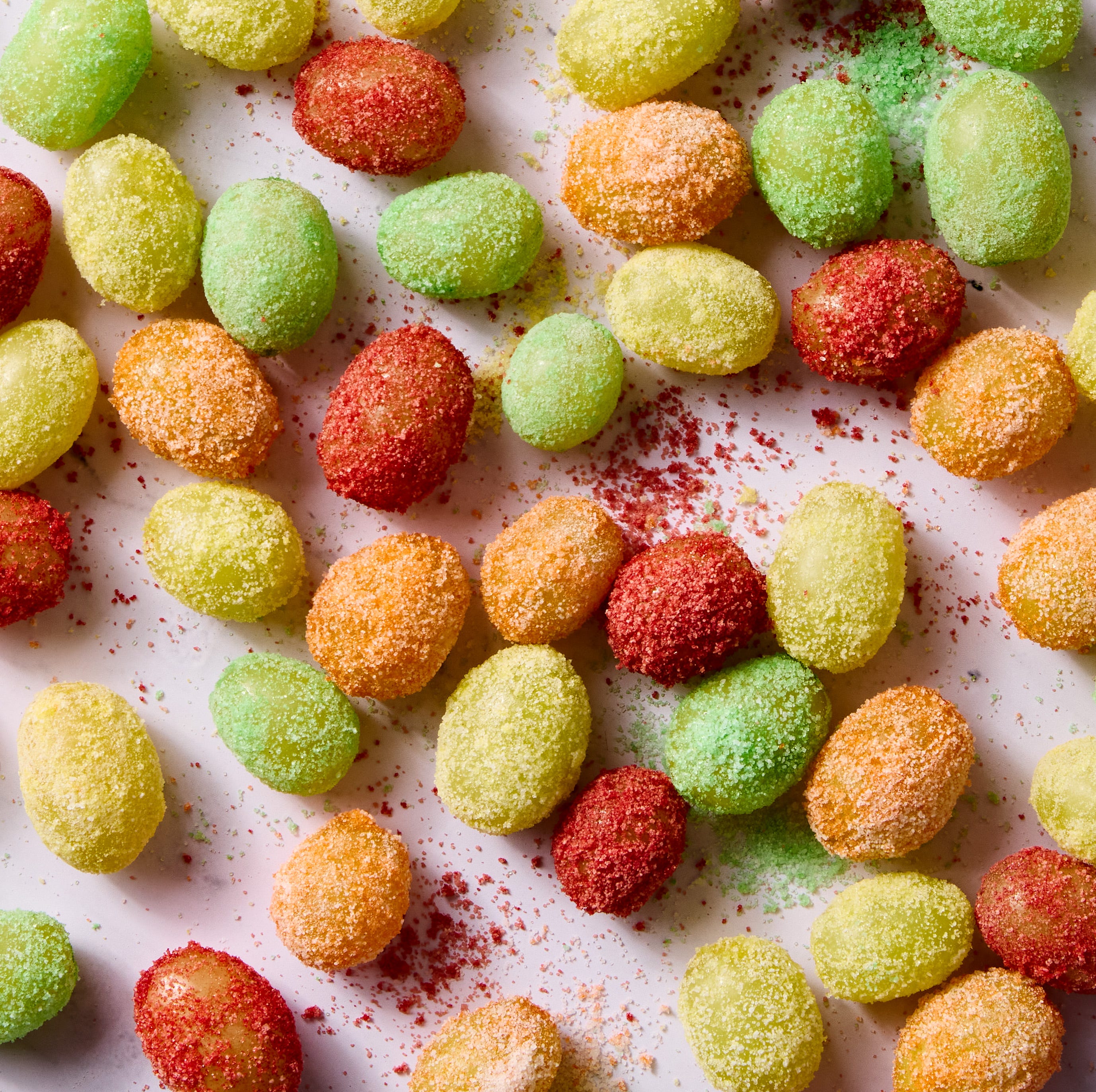red, yellow, and green colored sour patch green grapes on a light pink background