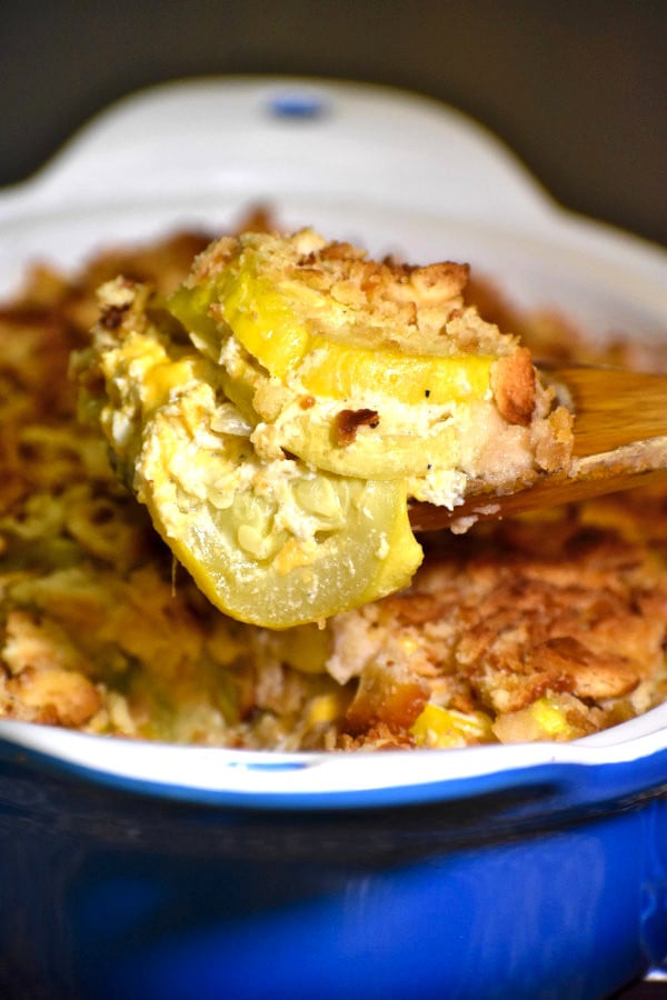 wooden spoon scooping a helping of southern squash casserole out of a blue dish