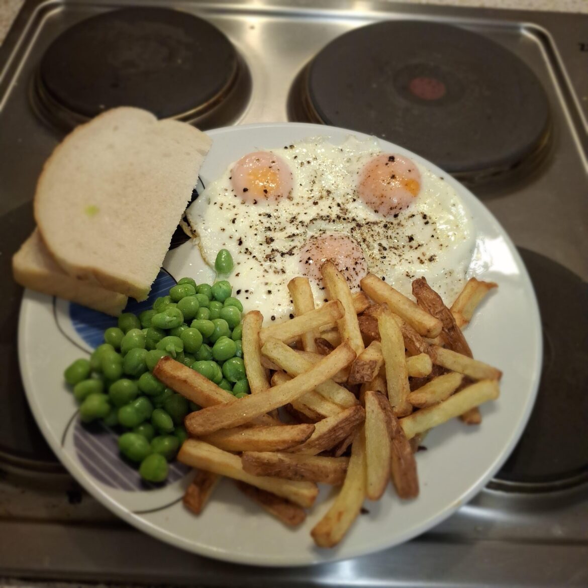 Homemade chips, eggs, peas and a slice of bread and butter.