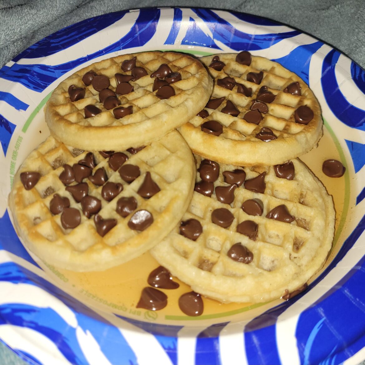 Four eggo waffles sitting in syrup covered in microwaved chocolate chips