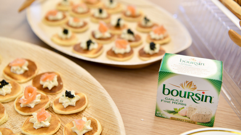 box of boursin cheese next to blini appetizers