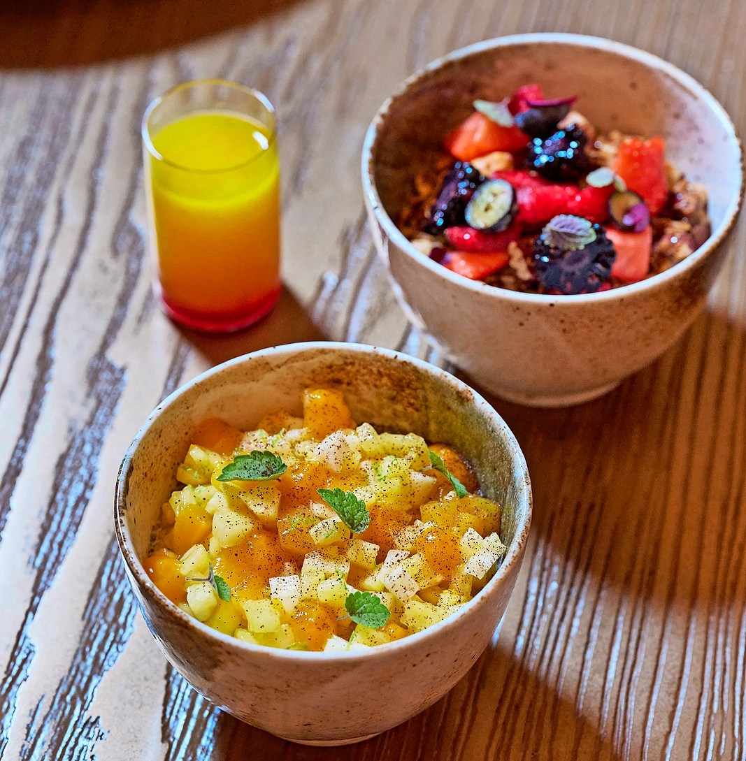 Two bowls of fruit, one with mixed berries and the other with diced fruit, with a glass of orange juice.