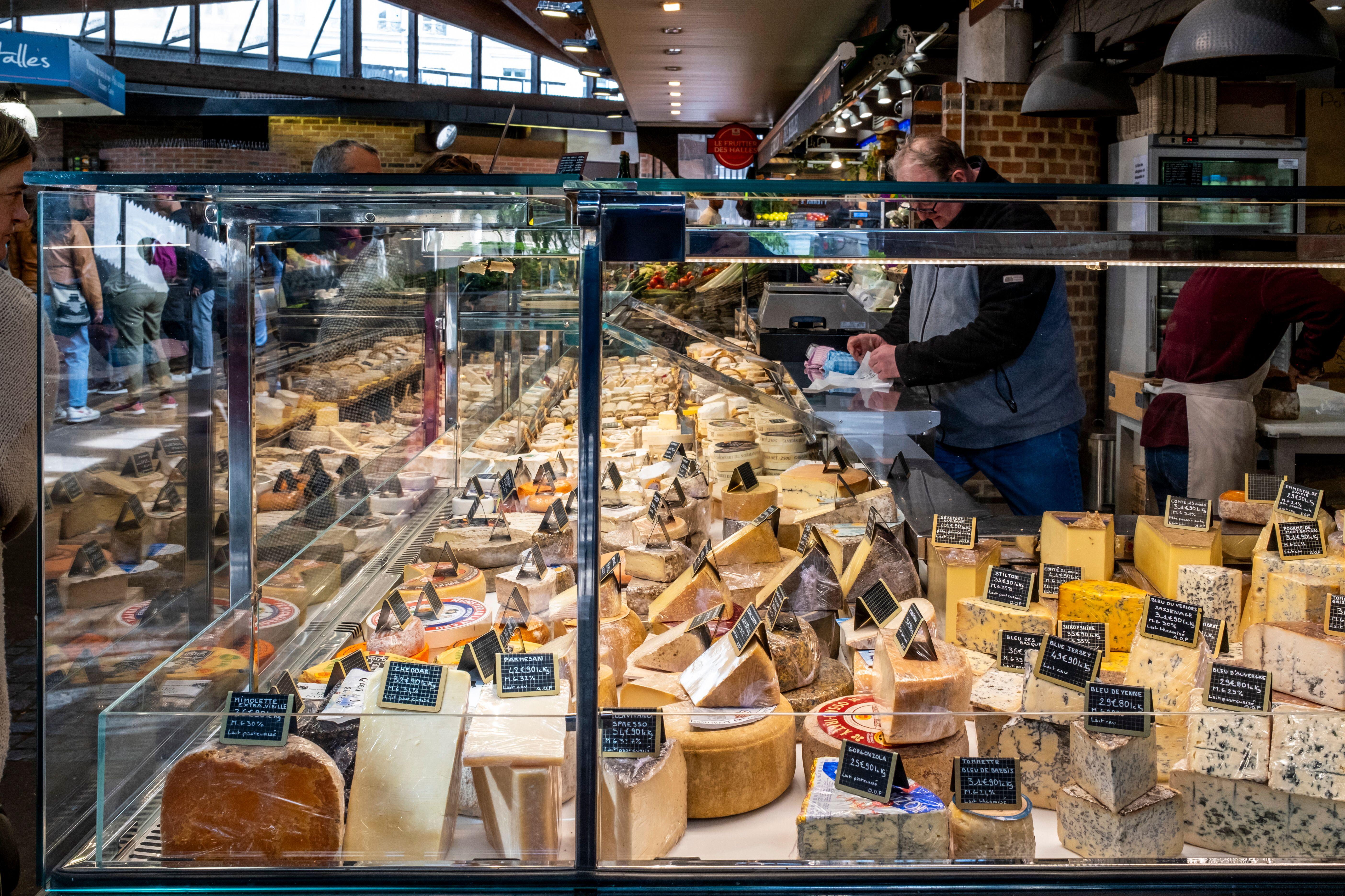 A colorful cheese shop inside Hallette du Vieux Marche indoor market in Rouen, Normandy, France, with a variety of cheeses on display in a glass case.