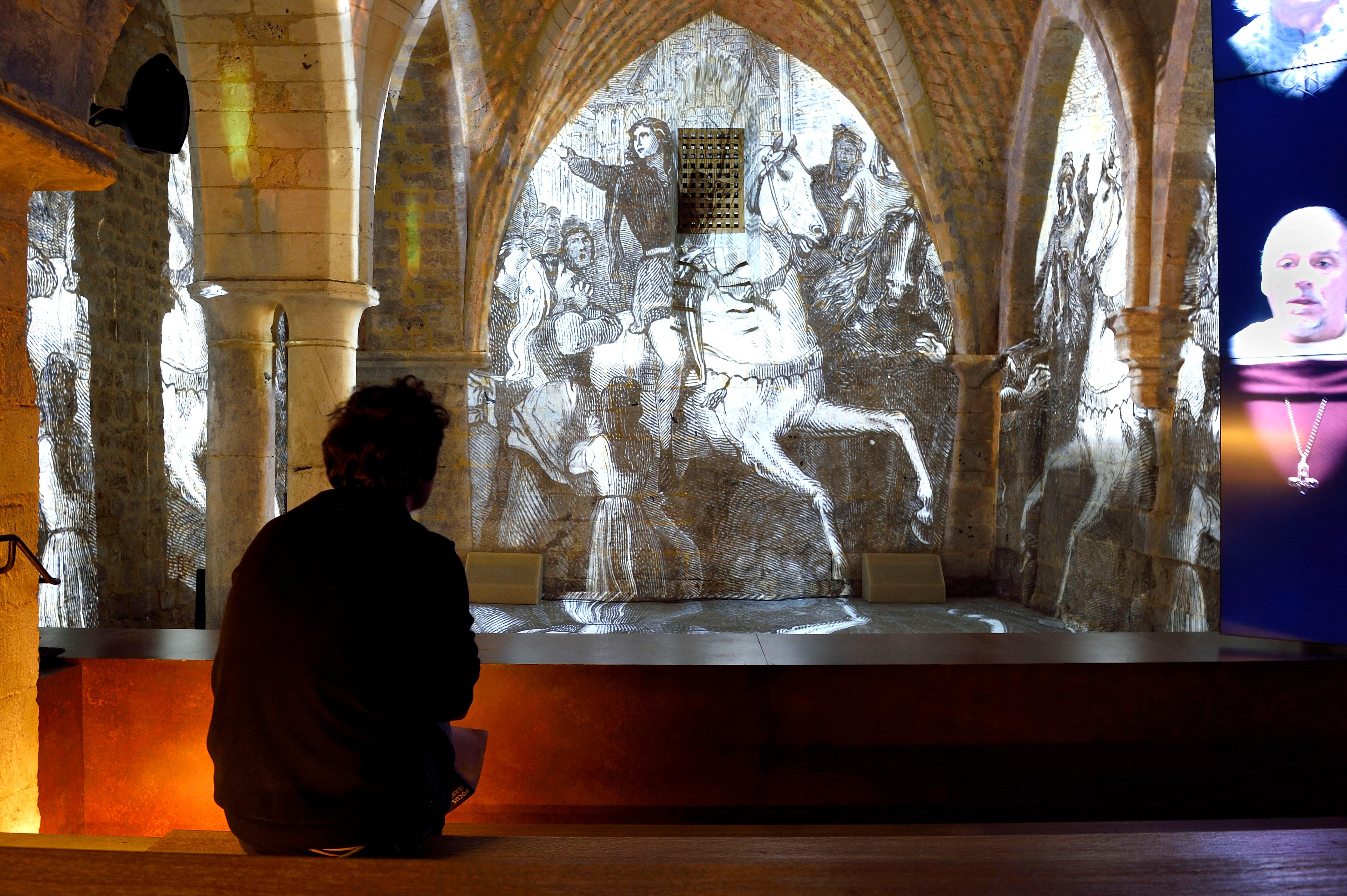 A person watching projections of images in the Gothic crypt of the Historial Joan of Arc Museum.