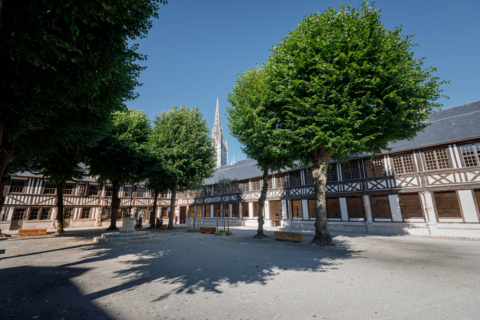 Aitre Saint-Maclou, a historical building in Rouen, France, featuring a courtyard with trees and a prominent steeple in the background.