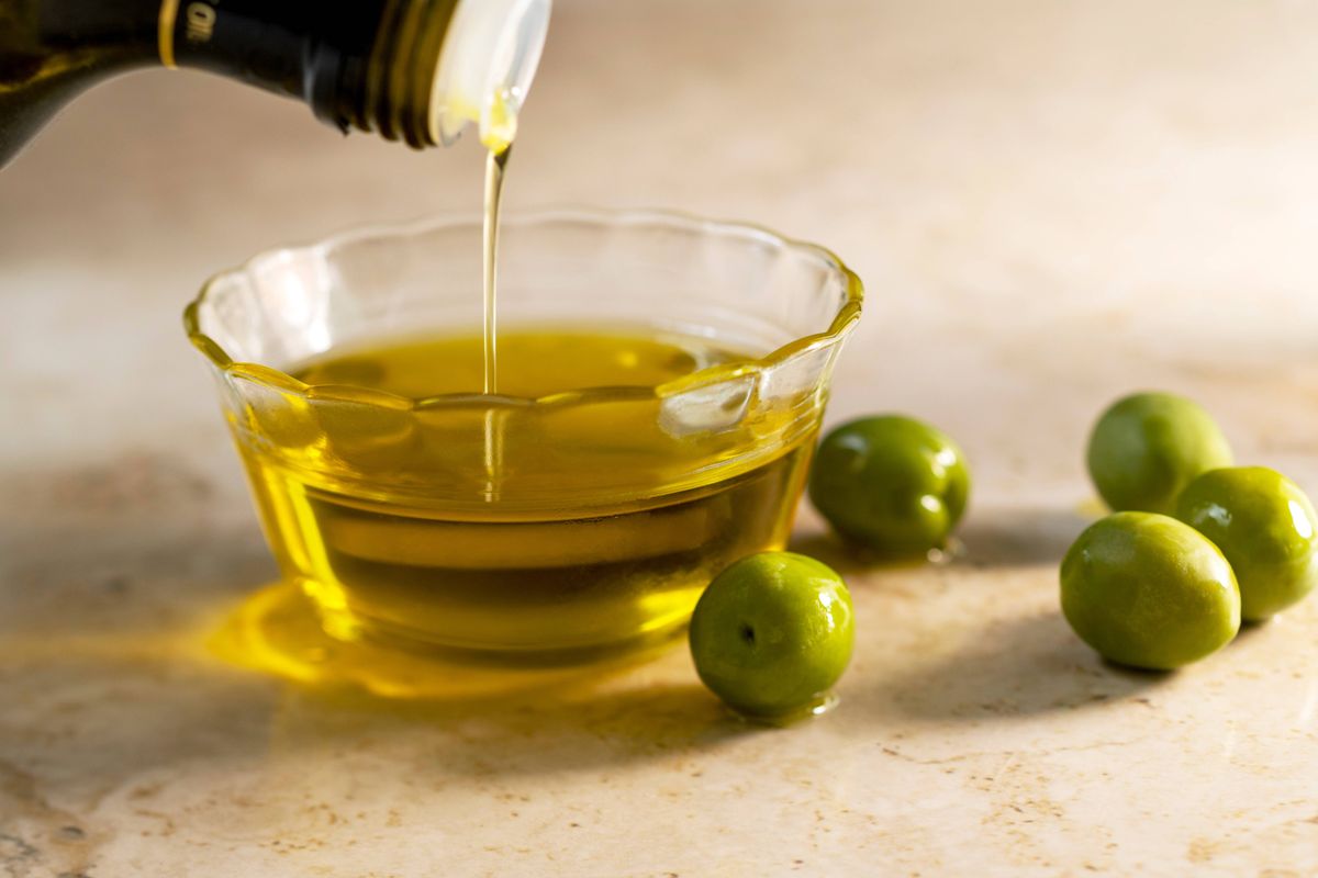 USA, Florida, Boca Raton, Olive oil pouring into small glass bowl with olives on table