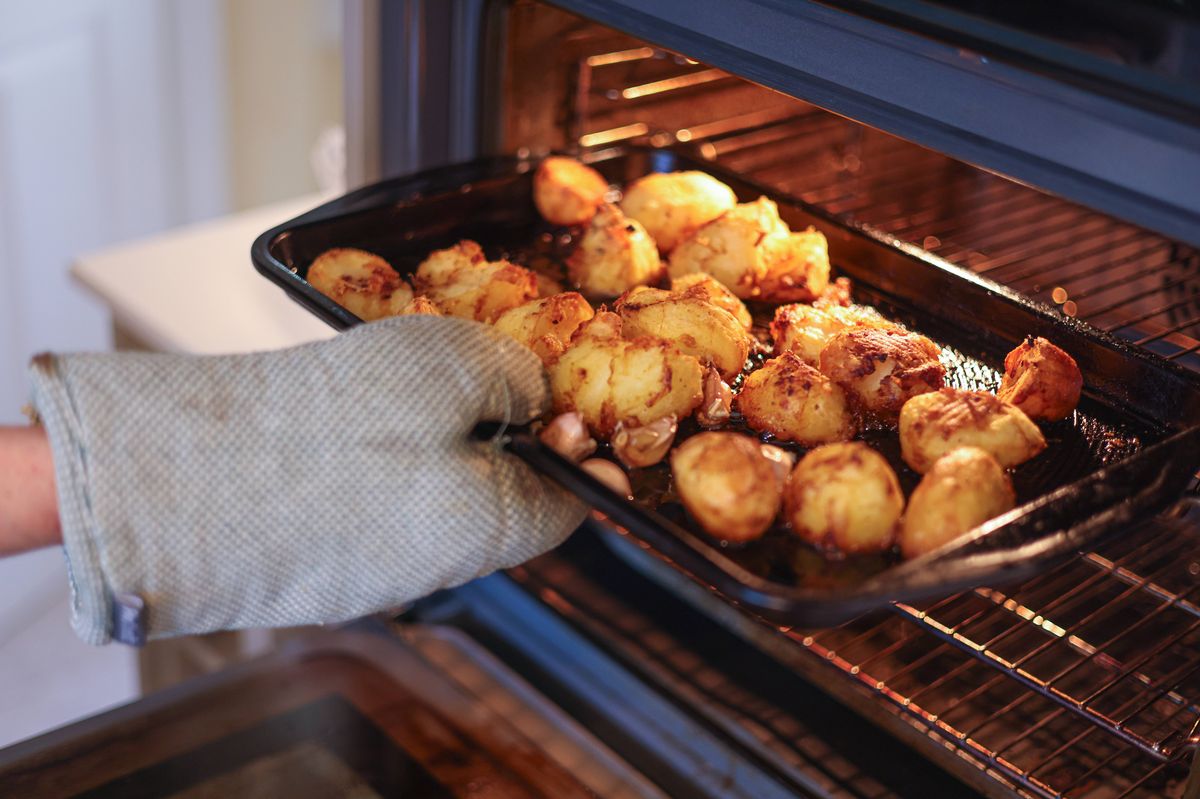 Taking hot crispy roast potatoes out of the oven