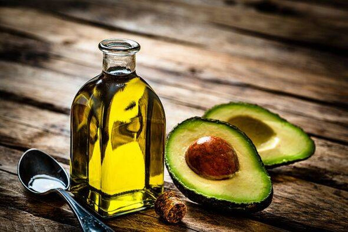 Vegan food: extra virgin avocado oil in a glass bottle shot on rustic wooden table. Sliced organic avocado and a spoon filled wi