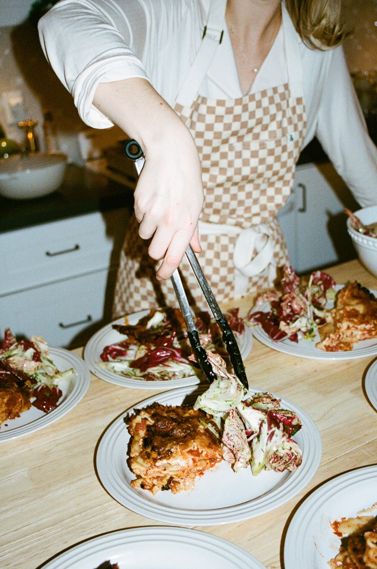 A woman wearing an apron places salad on a plate with chicken. 