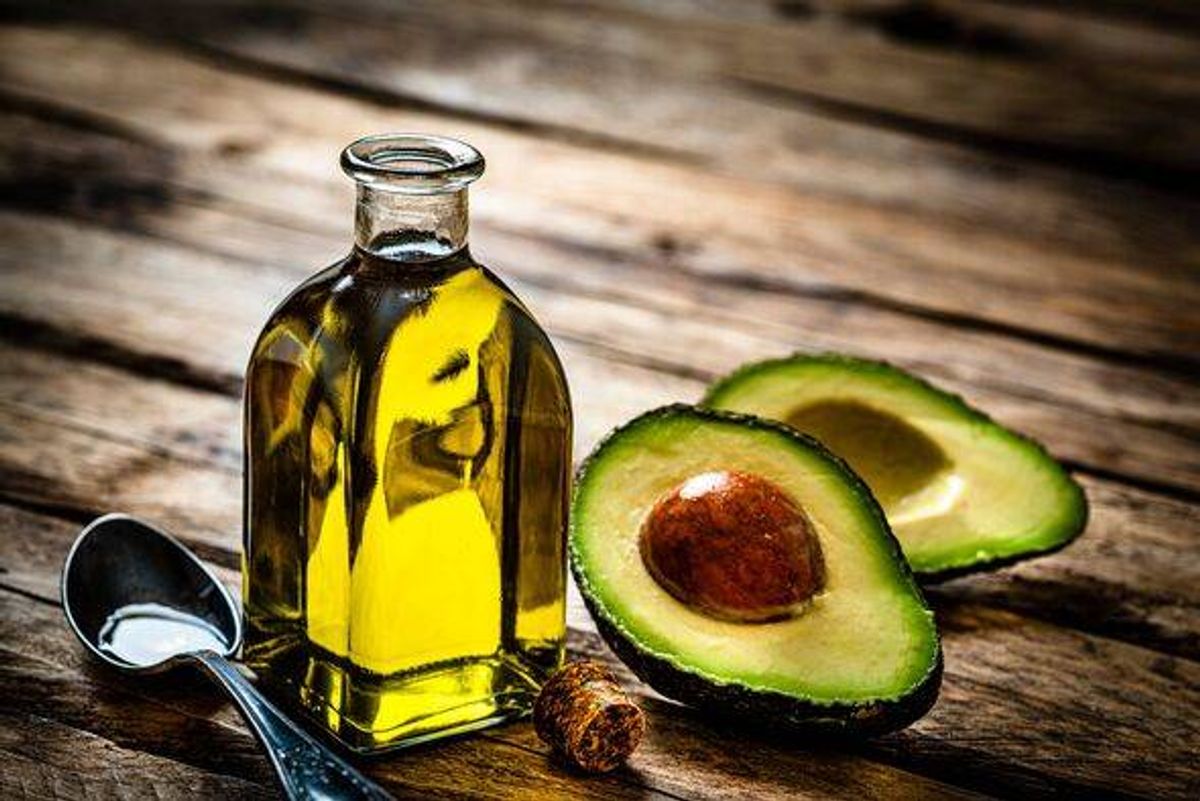 Vegan food: extra virgin avocado oil in a glass bottle shot on rustic wooden table. Sliced organic avocado and a spoon filled wi